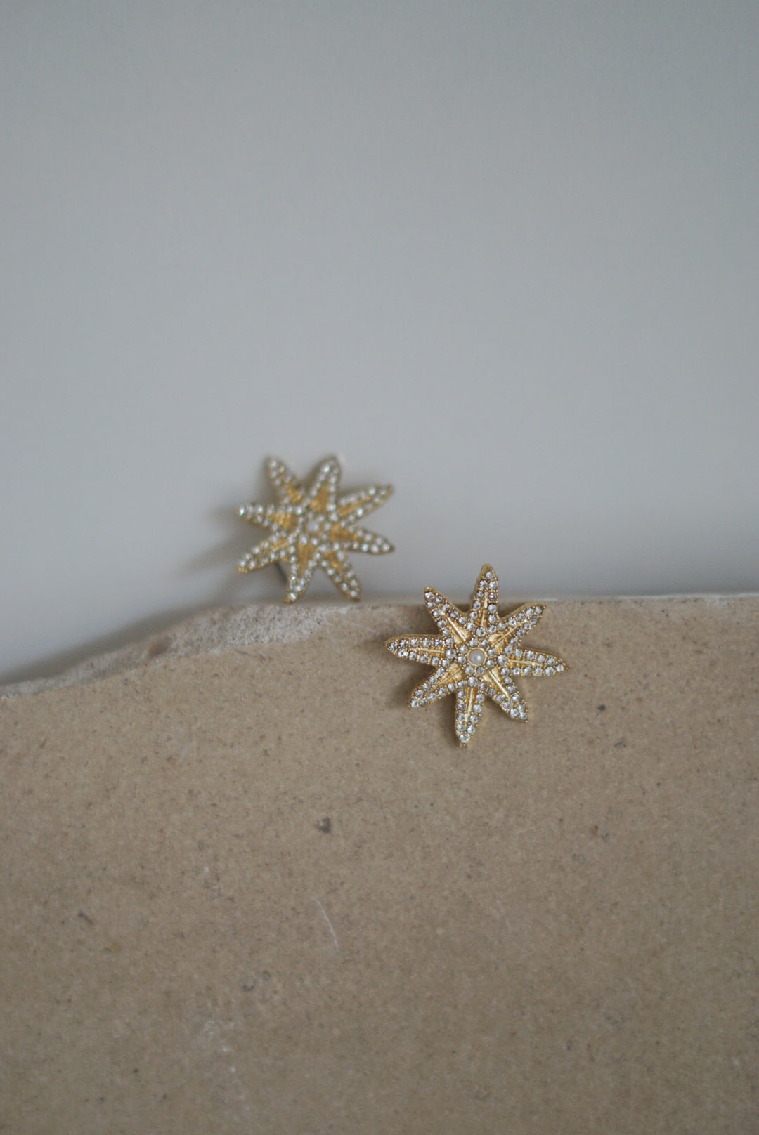 Acessório Brincos Noiva ou Convidada, em forma de estrela e Dourado. Acompanha com pedras brilhantes e uma pérola pequenina no centro. A imagem apresenta duas estrelas.